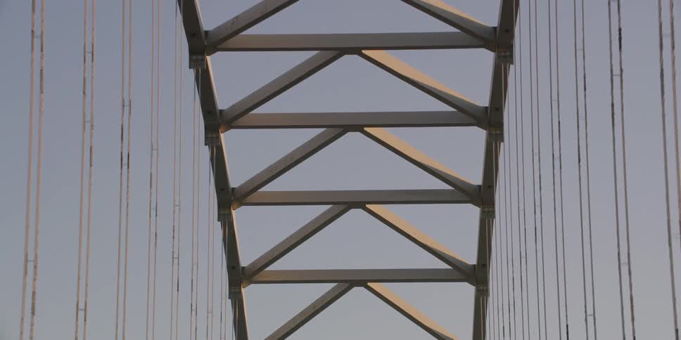 A slow tilt down from the American and Oregon flags atop the iconic Fremont Bridge, revealing its intricate steel architecture and highway signs