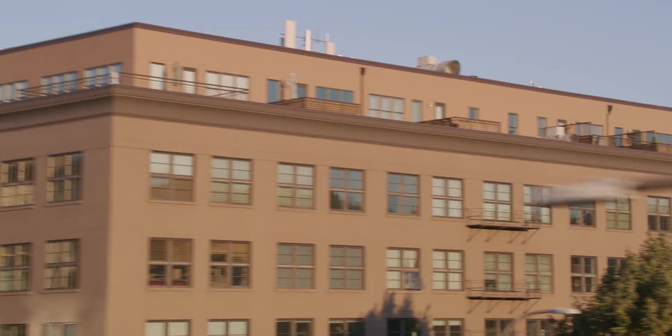 A slow tracking shot passes by the industrial and residential buildings of a city with the downtown skyline and a water tower in the background