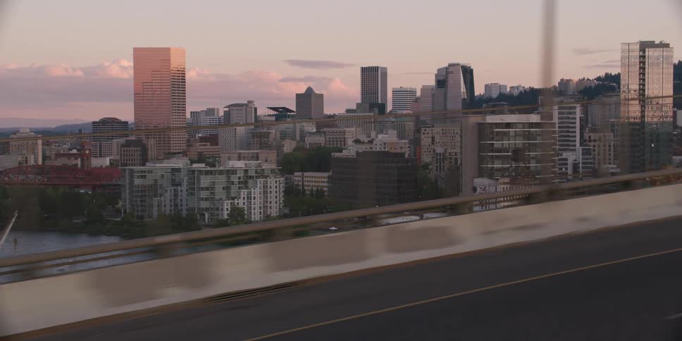 A slow-motion side-view shot from a vehicle driving over a bridge reveals the Portland, Oregon cityscape at golden hour