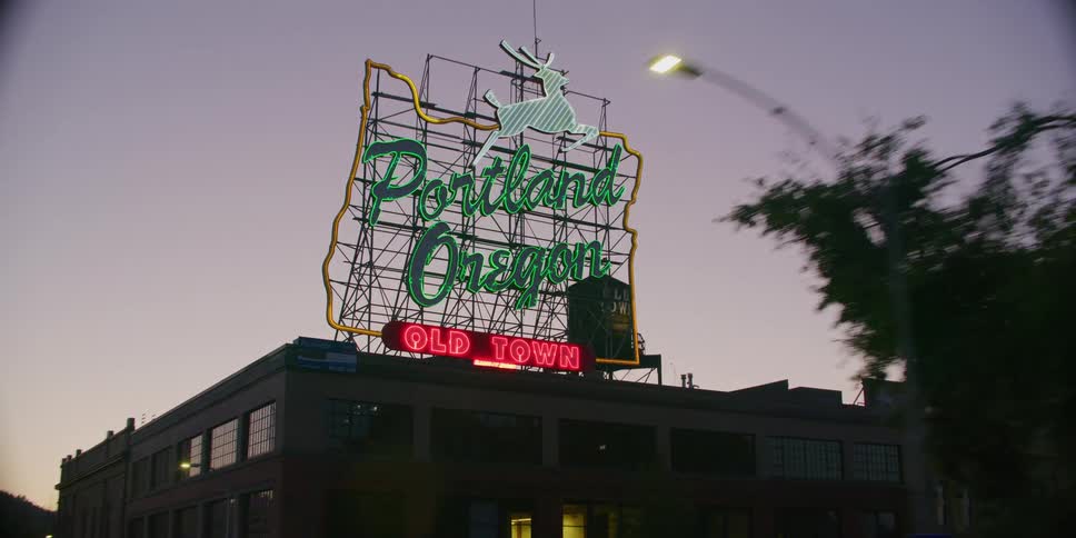 A smooth tracking shot captures the iconic 'Portland, Oregon' neon sign illuminating the sky at dusk