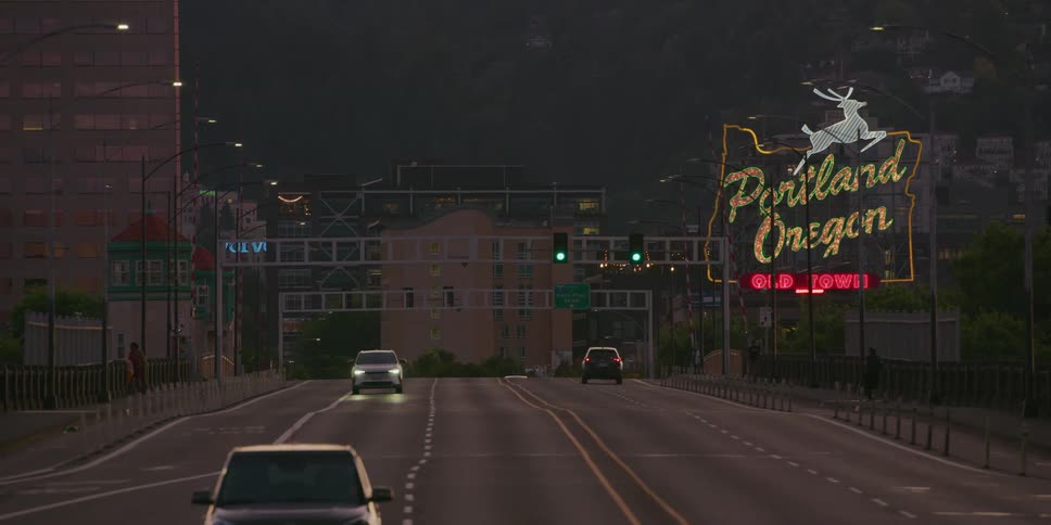Cars drive along the Burnside Bridge towards the iconic neon Portland, Oregon sign as the camera slowly pulls back at twilight