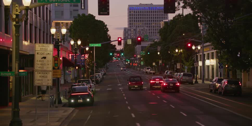 Cars wait at a red light on East Burnside Street in downtown Portland as dusk settles, then drive forward when the light turns green