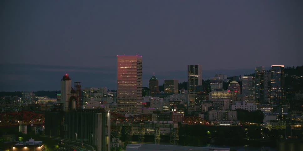 An aerial reveal of the Portland, Oregon city skyline at dusk, panning across industrial buildings and the Willamette River