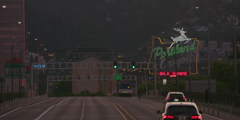 The famous Portland Oregon sign lights up the early morning sky as a city bus and a few cars travel across the bridge into town