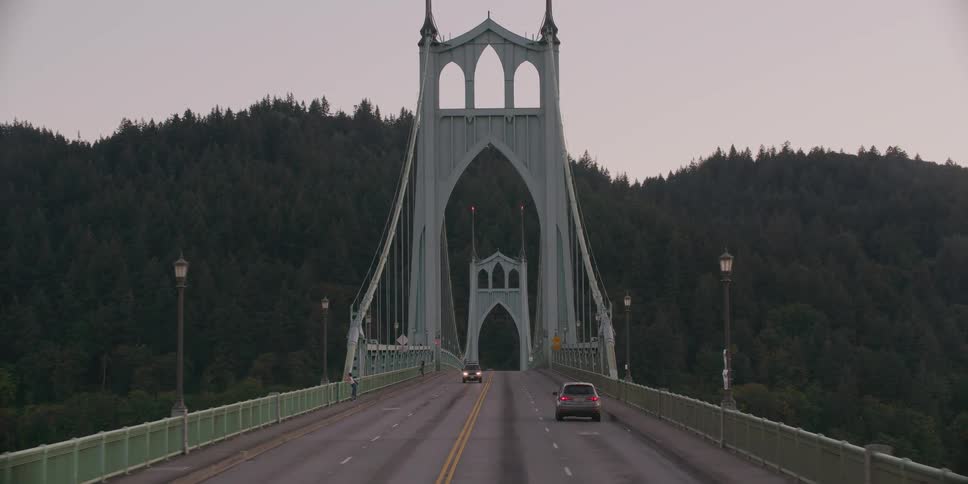 A slow, forward-moving shot captures cars driving across the iconic St. Johns Bridge in Portland, Oregon, on an overcast day