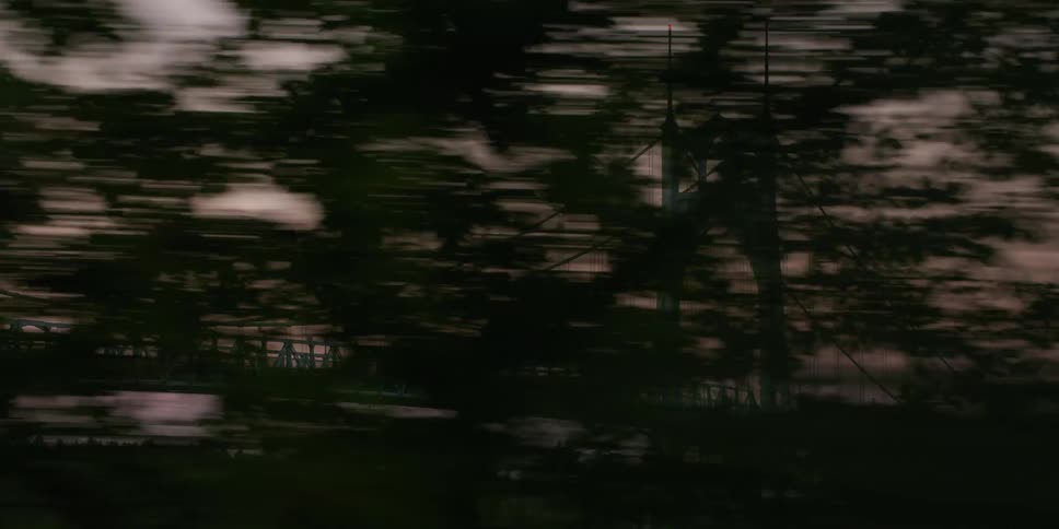 A dreamy, fast-moving tracking shot reveals the iconic St. Johns Bridge through a blur of silhouetted trees at sunset
