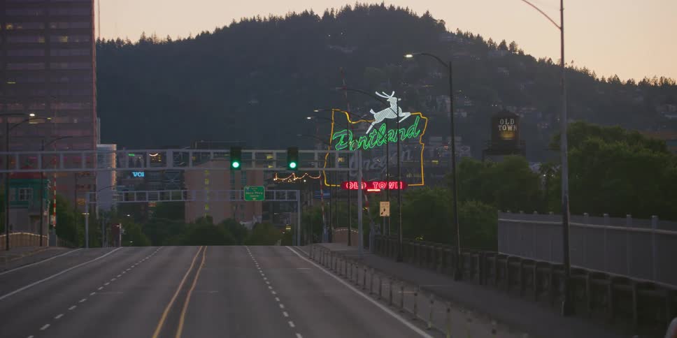 Slowly approaching the iconic 'Portland Oregon Old Town' neon sign at dusk on a quiet city bridge
