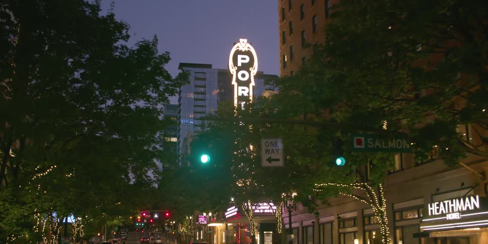 Slow push-in shot of the iconic glowing Portland sign on a downtown city street at dusk