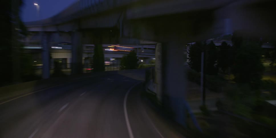 A point-of-view perspective driving on a bustling city highway at twilight, passing under overpasses and following traffic