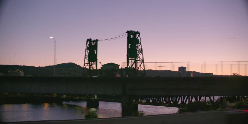 Driving past Portland, Oregon's iconic Steel Bridge and city skyline silhouetted against a beautiful sunset sky