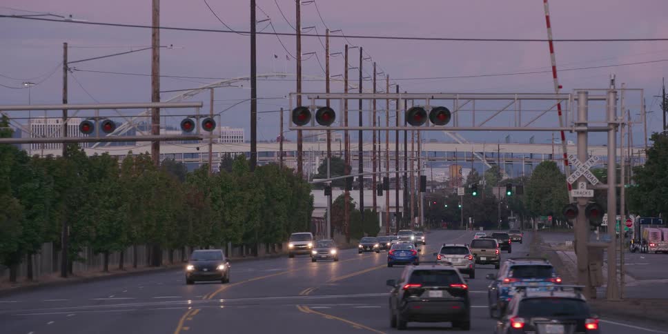 Slow zoom shot of commuter traffic driving along an industrial road towards a railroad crossing at dusk