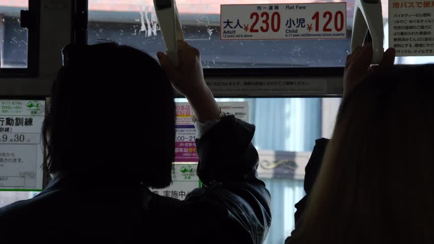 Silhouetted passengers hold onto handles while commuting on a public bus through a city in Japan