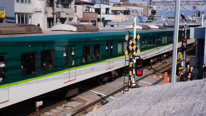 A green and white passenger train travels along the tracks through a station in an urban city in Japan