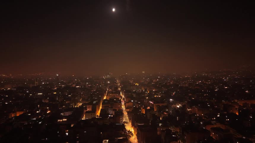A nighttime timelapse from an aerial perspective shows the bustling city streets under a bright full moon