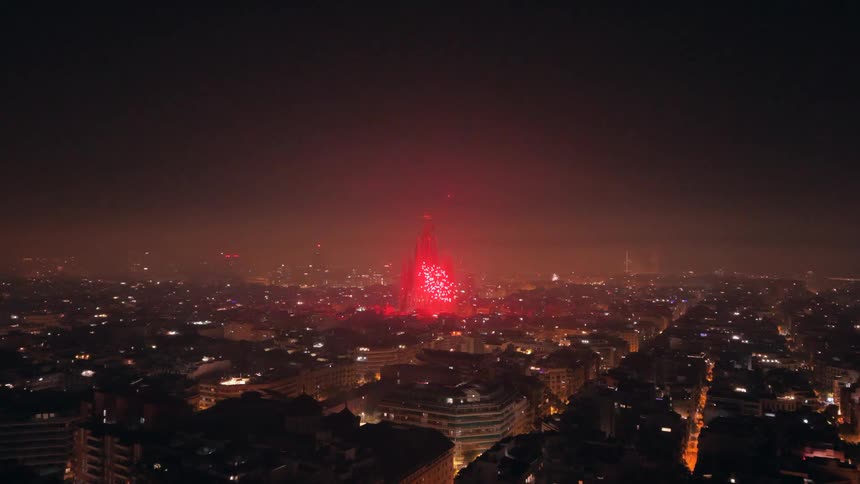 Fireworks erupt over the sprawling city of Barcelona at night, culminating in a spectacular red light show on the Sagrada Família cathedral