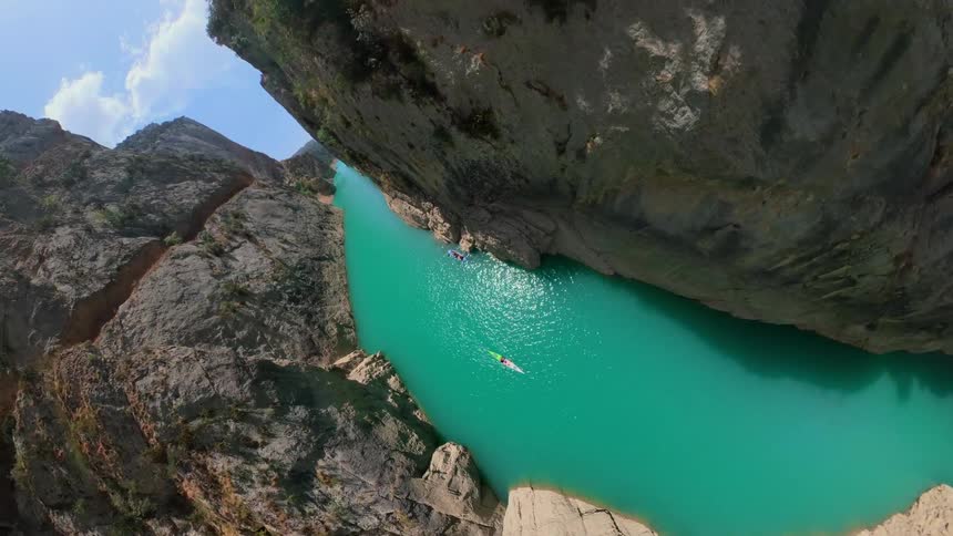 A stunning FPV drone flight navigates through a massive, narrow canyon with vibrant turquoise water and tiny kayaks below