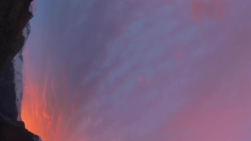 A cinematic FPV drone flight through a spectacular mountain valley at sunset captures the vibrant, colorful sky and the last light on the snow-capped peaks