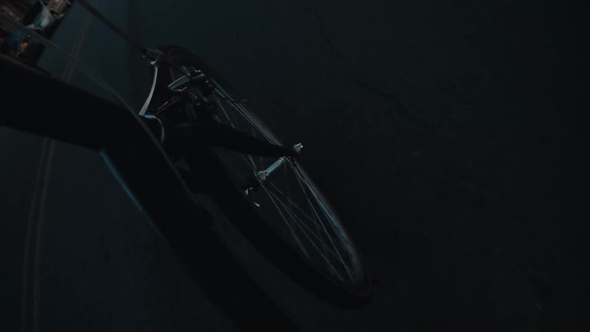 A unique POV shot captures a bicycle's front wheel and the cyclist's shadow while riding through city streets from day into night