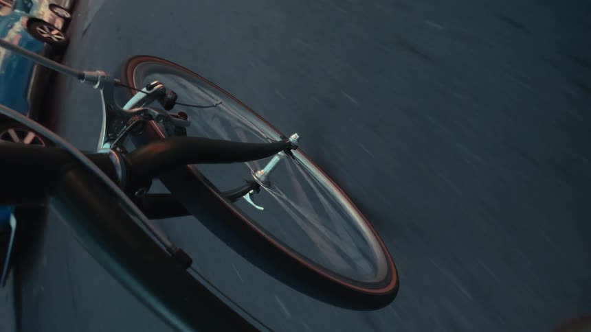 A point-of-view time-lapse captures a bicycle's front wheel spinning along a city street as the day transitions into night
