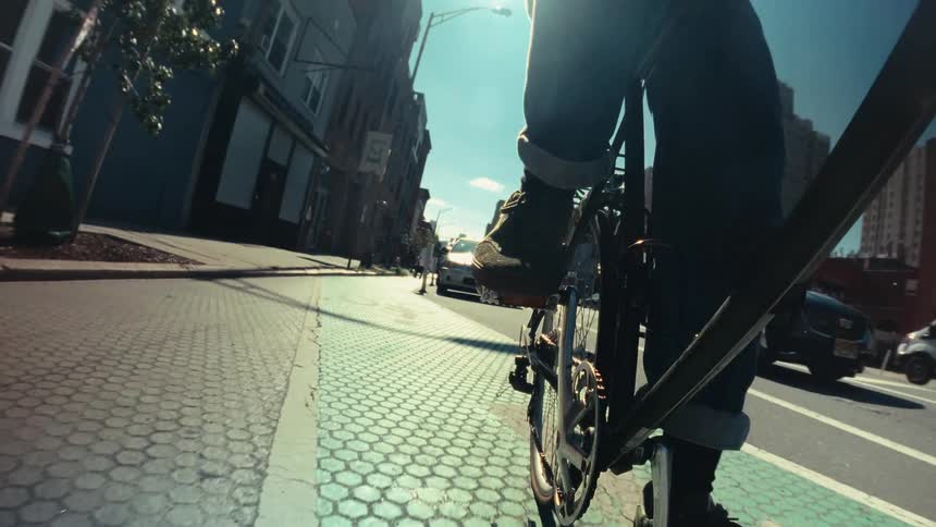 Cinematic low-angle slow-motion footage shows a person cycling down a sun-drenched city bike lane