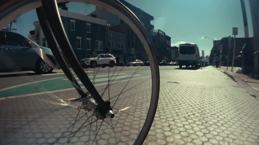A unique point-of-view shot of a bicycle wheel spinning while riding through a green bike lane in the city on a sunny day