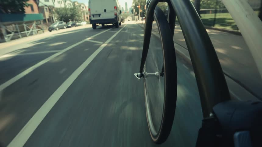 An immersive first-person view from a bicycle speeding down a dedicated city bike lane next to traffic on a sunny day