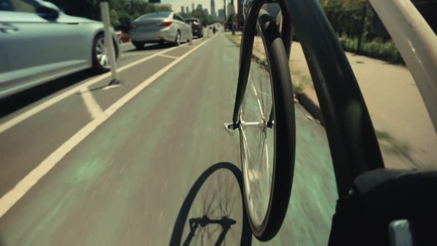 Dynamic point-of-view shot of a bicycle wheel spinning while riding at speed through a city bike lane towards the skyline