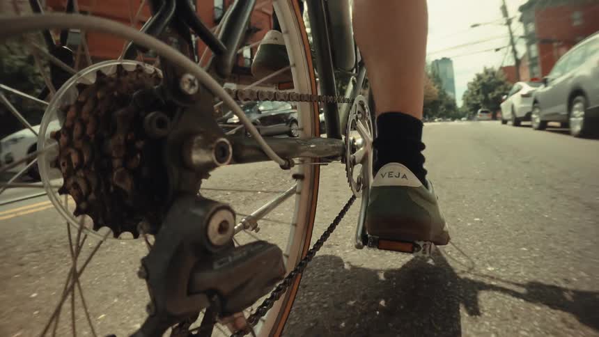 Dynamic low-angle shot captures the turning gears and pedals of a bicycle commuting down a sunny city street in slow motion