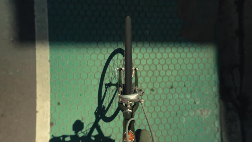 A first-person point of view of a bicycle's front wheel rolling down a sunny, paved city street and into a green bike lane