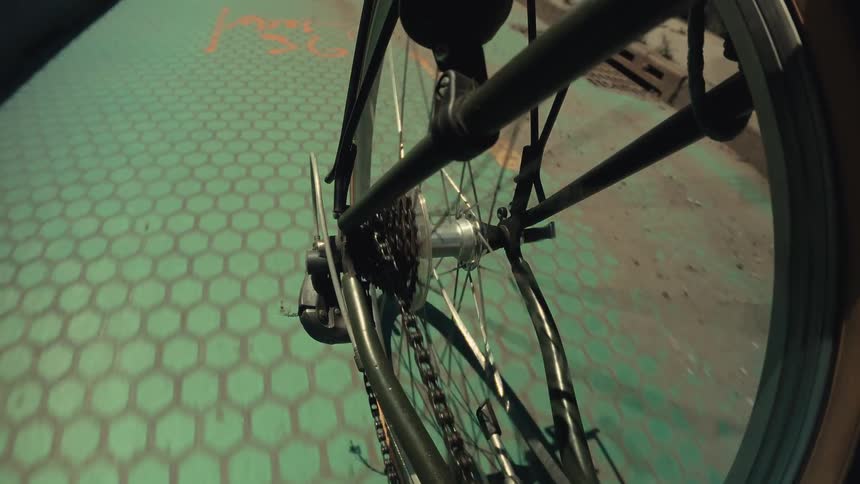 A unique timelapse point-of-view shot of a bicycle's back wheel and chain spinning while riding along a green bike lane from day into night