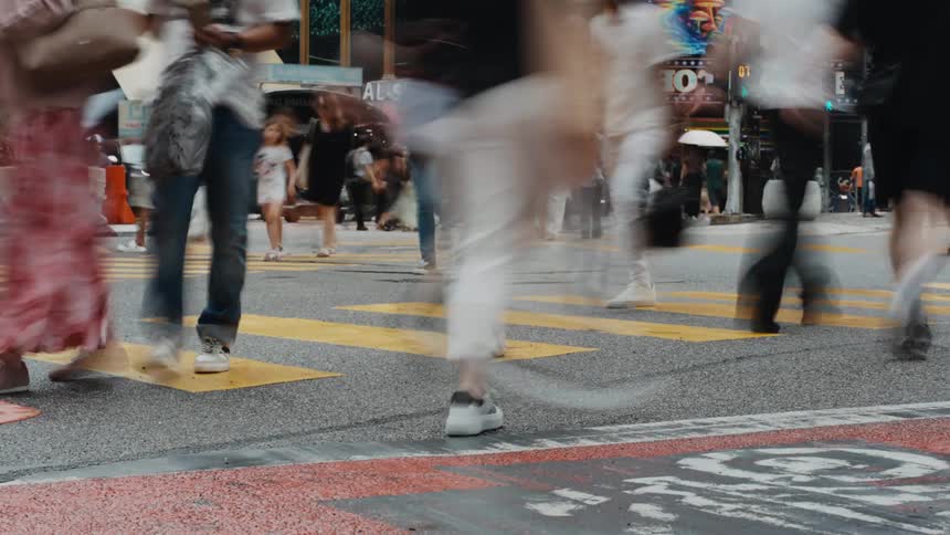 A low-angle, long-exposure time-lapse captures the blurred motion of a diverse crowd of pedestrians crossing a busy city street