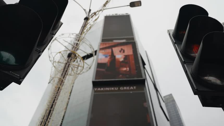 Low-angle view of city traffic lights changing as the camera pans to reveal a tall building with large digital screens