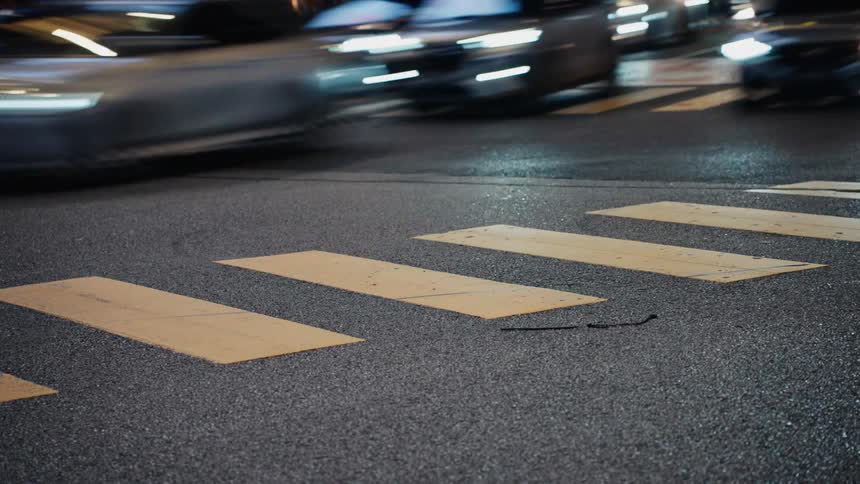 A long exposure shot of traffic blurring past a yellow crosswalk on a city street at night