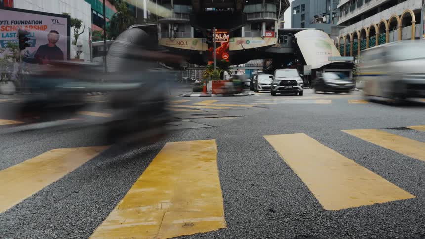 A dynamic time-lapse from a low angle captures the frenetic energy of a busy city intersection as traffic blurs past a yellow crosswalk