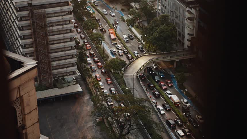 A high-angle view from a skyscraper shows a busy city highway with congested traffic on a rainy day