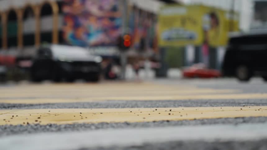 A low-angle, shallow-depth-of-field shot of a yellow crosswalk with blurred city traffic moving in the background