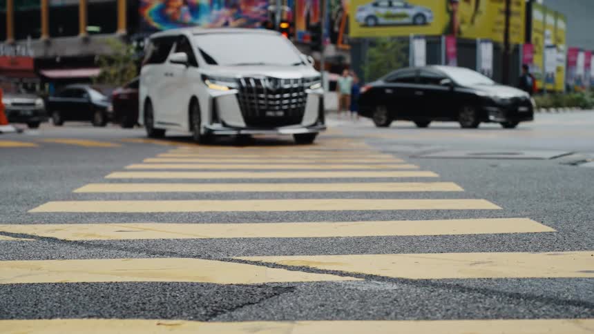 A slow-motion, low-angle shot focuses on a yellow crosswalk as blurred city traffic and pedestrians move in the background