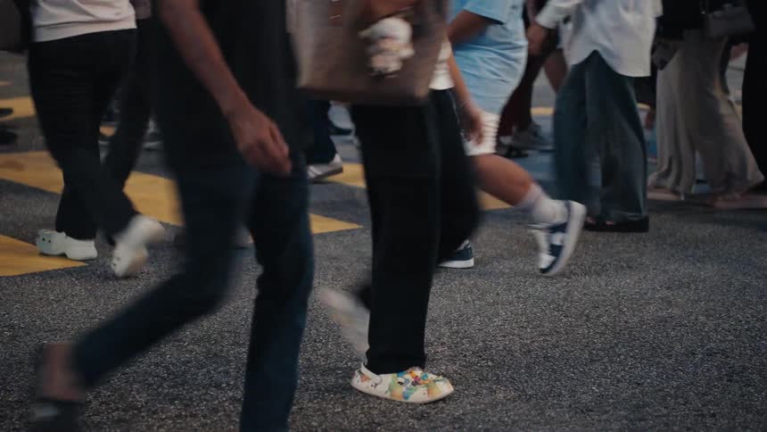 A low-angle, slow-motion view of a diverse crowd of pedestrians' feet crossing a city street at night