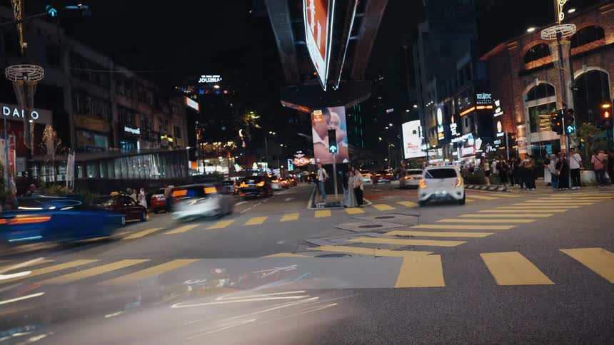 A long-exposure time-lapse captures the vibrant energy of a city intersection at night, with traffic creating colorful light trails