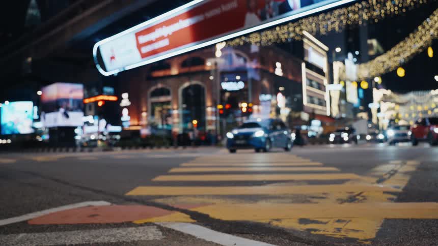 Defocused traffic passes over a yellow crosswalk at a busy city intersection illuminated by neon lights at night
