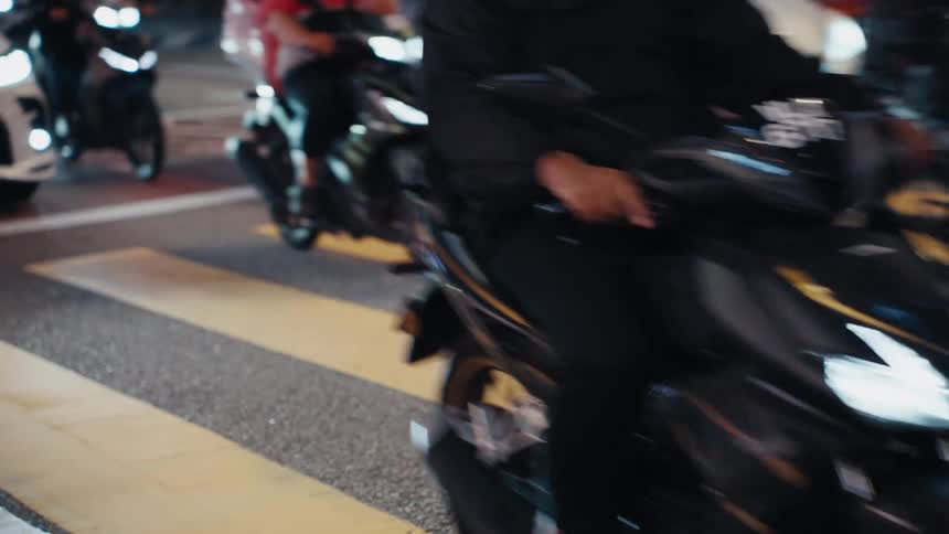 Slow motion close-up of motorcycle and car traffic crossing a yellow crosswalk at night in a bustling city