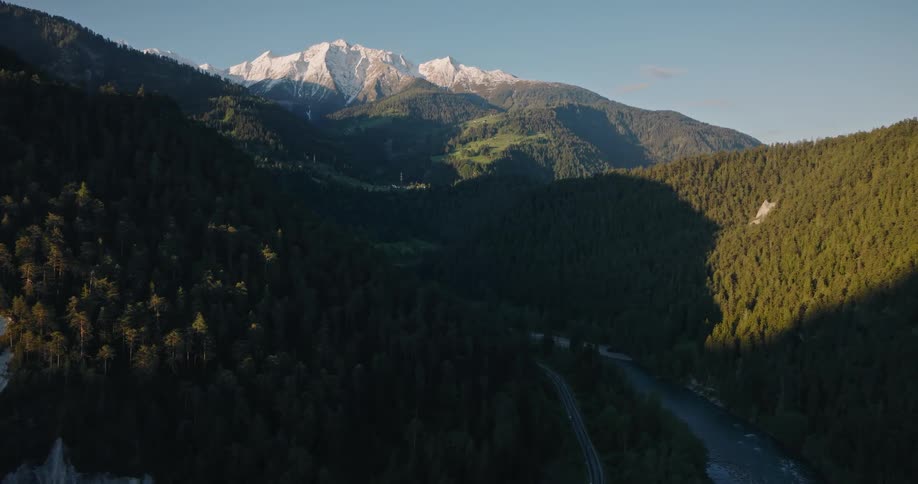 Aerial view of a lush green valley and river with majestic snow-capped mountains in the background at sunrise