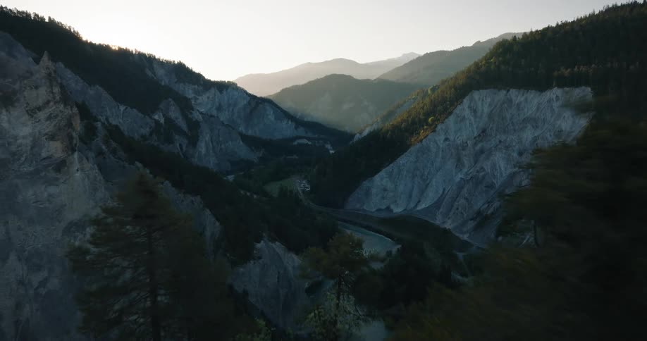 An aerial view pulls back over pine trees revealing a dramatic mountain gorge and river valley at sunrise
