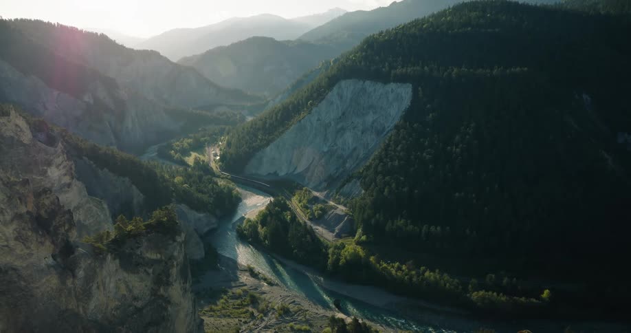A stunning wide view of a turquoise river winding through a deep mountain gorge during a hazy sunrise