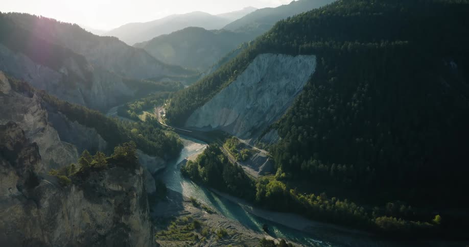 A stunning aerial view of a vast mountain canyon with a turquoise river winding through the valley at sunset