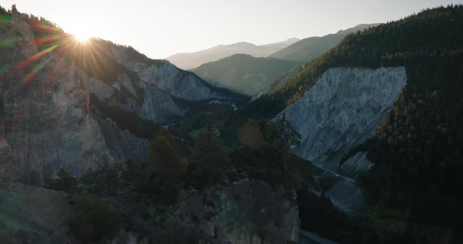 Aerial drone pulls back to reveal a majestic mountain canyon as the sun flares over the horizon at sunrise