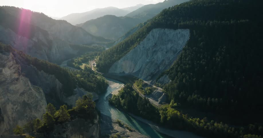 Breathtaking aerial pull-back shot of a turquoise river winding through a majestic, forested mountain canyon at sunrise