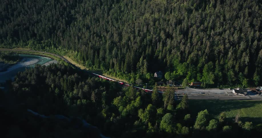 A stunning aerial view from a mountain reveals a red passenger train traveling through a vast, dense green forest valley