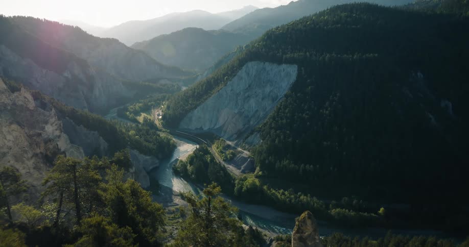 An epic aerial shot pulls back to reveal a majestic mountain valley with a winding river and a train passing through at sunrise