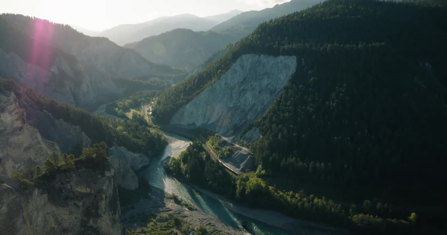 A breathtaking, static shot captures a train traveling through a majestic mountain canyon alongside a winding river at sunset
